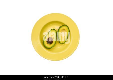 Avocado in zwei Scheiben in einer gelben Platte. Frischer Avocado isoliert auf weißem Hintergrund. Gesundes Esskonzept. Draufsicht, flacher Lay. Stockfoto