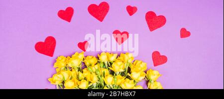 Banner Gelb Rosa Rosen Blumen mit roten Herzen auf violettem Tischhintergrund Draufsicht mit freiem Platz Kopierraum Stockfoto