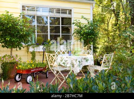 Vorhalle mit weißem Café-Tisch und Stühlen, roter Wagen mit Blumen Stockfoto