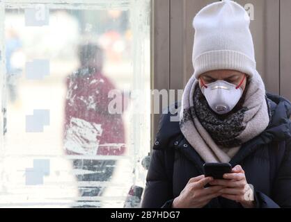 Berlin, Deutschland. März 2020. Eine junge Frau, die eine Schutzmaske trägt, holt mit ihrem Smartphone Informationen über die Nachrichtensituation und weitere Entwicklungen zum Corona-Virus am Alexanderplatz im Bezirk Mitte ein. Kredit: Wolfgang Kumm / dpa / Alamy Live News Stockfoto