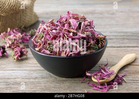 Gesunde Echinacea Blumen in schwarzer Keramikschale und Sack trockener Koneblumen auf dem Hintergrund. Pflanzenheilkunde. Stockfoto