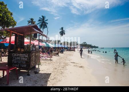 Cocktailstände und Liegestuhl am belebten, weiß geschliffenen Strand und türkisfarbenem Wasser der Baru Island vor der karibischen Küste von Cartagena, Kolumbien Stockfoto