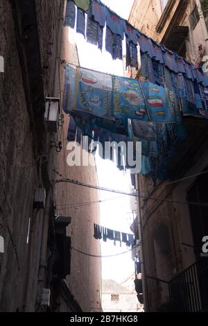 Uniformen und Schals des FC Neapel werden vor einem Fenster in der Innenstadt von Neapel gehängt Stockfoto