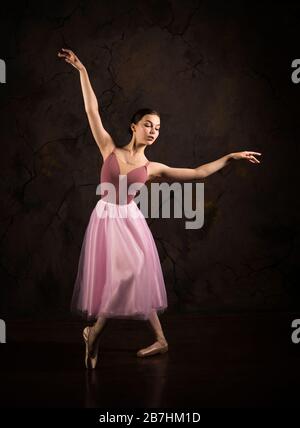 Eine schlanke Frau in einem rosa Rock und beige Top tanzen Ballett. Studio-Aufnahmen vor dunklem Hintergrund, isolierte Bilder. Stockfoto