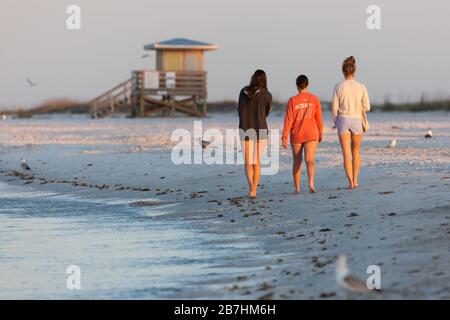 Drei Frauen gehen am Strand in Lido Key, der am 16. März 2020 von der Morgensonne in Sarasota FL, USA angezündet wird. Stockfoto
