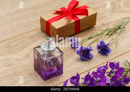 Flasche Parfüm, Geschenkbox mit rotem Band und Sterndistelblüten auf den Holzbrettern. Konzept, an Feiertagen ein Geschenk zu machen. Draufsicht. Stockfoto