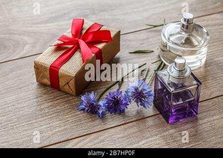 Geschenkschachtel mit rotem Band und Flaschen Parfüm auf Holzbrettern, die mit Knabberblüten verziert sind. Draufsicht. Stockfoto
