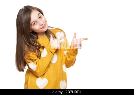 Schönes junges Mädchen im senfgelben Pullover mit Blick auf die Kamera, lächelnd und zur Seite zeigend. Studio mit Taille oben, aufgenommen auf weißem Hintergrund. Stockfoto