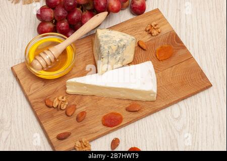 brie Käse und roquefort auf einem Brett mit Honig, Trauben, getrockneten Aprikosen und Nüssen Stockfoto