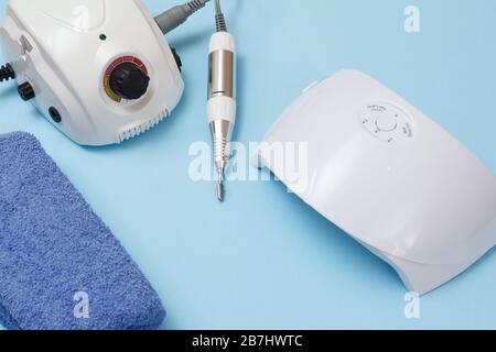 Fräser, LED UV-Lampe und Handtuch auf blauem Hintergrund. Eine Reihe von kosmetischen Tools für professionelle Hardwaremaniküre. Draufsicht. Stockfoto