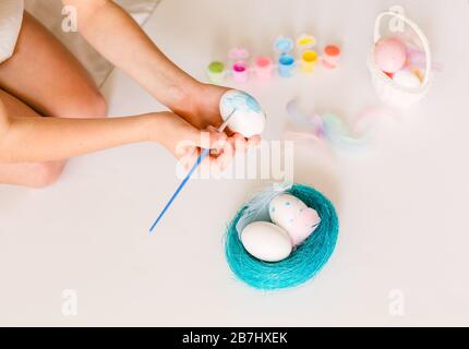 Kleines Mädchen färbt ostereier mit Farben und Bürste auf hellem Hintergrund. Ostern, Feiertage, Traditionkonzept Stockfoto