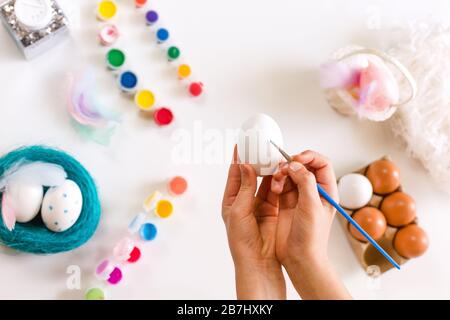 Nahaufnahme von Kinderhänden, die Ostereier mit Farben färben und auf hellem Hintergrund bürsten. Ostern, Feiertage, Traditionkonzept Stockfoto