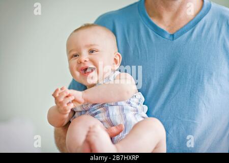 Baby lächelt, während es von seinem Vater gehalten wird. Stockfoto