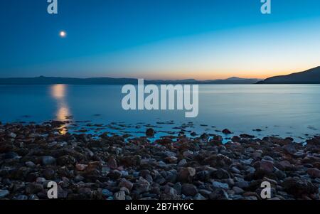 Die Insel Skye in der Dämmerung, Schottland. Der Mond steigt und die Sonne geht über die Insel Sky, von der Applecross Bay an der schottischen Westküste aus betrachtet. Stockfoto