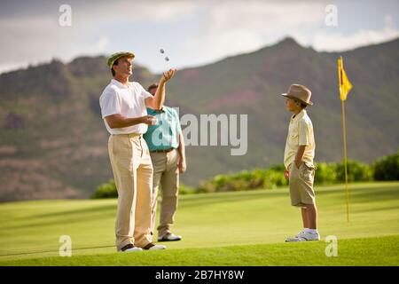 Der junge Junge beobachtet, wie sein Golfspielervater Golfbälle jongliert, während sie auf einem Grün stehen. Stockfoto