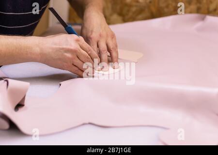 Schuhmacher repariert Schuh. Schuhmacher näht Schuhe. Schuhmacherwerkstatt. Schuhmacher schneidet Leder in einer Werkstatt. Modedesigner-Schuhe. Stockfoto