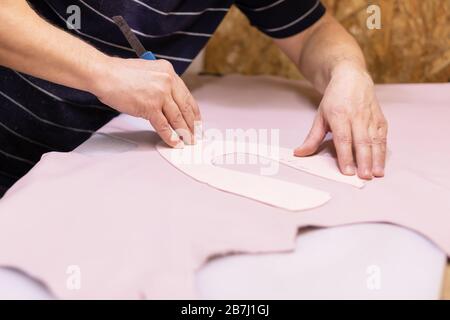 Schuhmacher repariert Schuh. Schuhmacher näht Schuhe. Schuhmacherwerkstatt. Schuhmacher schneidet Leder in einer Werkstatt. Modedesigner-Schuhe. Stockfoto