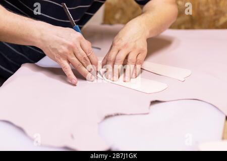 Schuhmacher repariert Schuh. Schuhmacher näht Schuhe. Schuhmacherwerkstatt. Schuhmacher schneidet Leder in einer Werkstatt. Modedesigner-Schuhe. Stockfoto