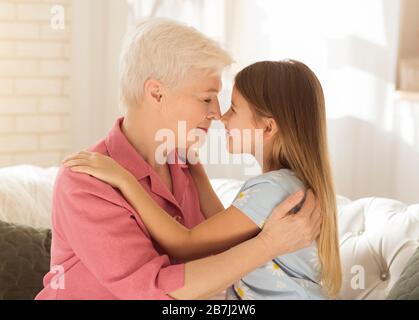 Liebliches kleines Mädchen und ihre Oma berühren Nasen und umarmen sich zu Hause Stockfoto