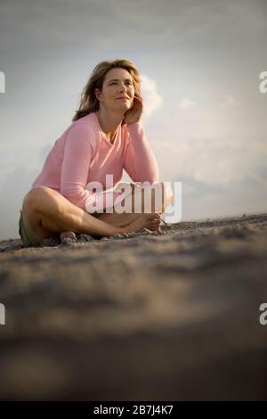 MittelErwachsene Frau, die mit gekreuzten Beinen an einem Strand sitzt. Stockfoto