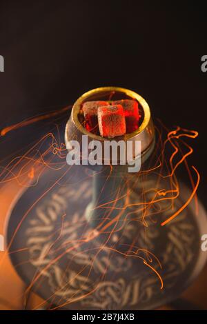Rote Funken von den Hookah-Kohlen, die um die Glühbirne fliegen. Rauchende Hookah in einem Barkonzept. Stockfoto