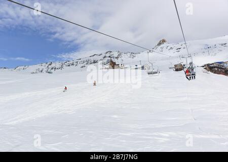 Eine zweisitzige Seilbahn und eine Skipiste mit Snowboardern im Skigebiet Dombay mitten in der Wintersaison. Sonniger Frosttag Stockfoto