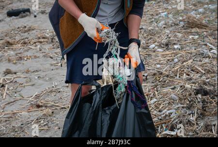 Ein Freiwilliger, der Müll am Strand pflückt und ihn in einen schwarzen Müllsack legt Stockfoto