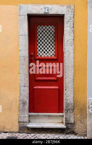 Detail der roten Tür, Steinmauer, Kopfsteinpflaster Bürgersteig in Lissabon, Portugal Stockfoto