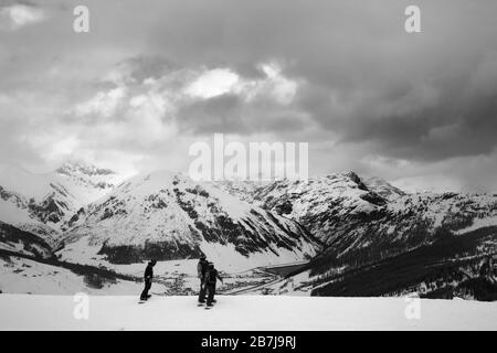 Die Gruppe der Snowboarder startet auf Abfahrt. Hohe Schneeberge und bewölkter Sturmhimmel im Winter vor blizzard. Italienische Alpen. Livigno Lombardei Stockfoto