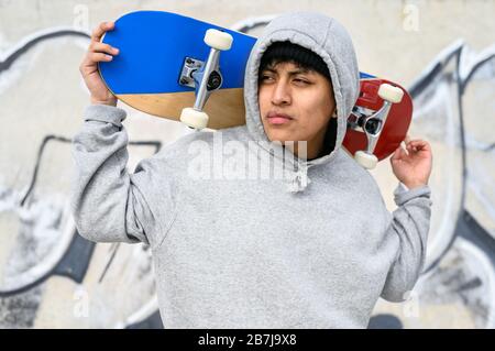 Junger lateinischer Skater-Mann posiert mit Skateboard im Skatepark. Stockfoto