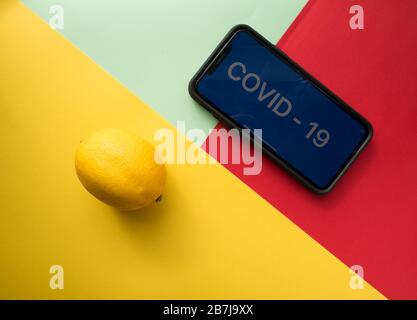 USA, 16. März 2020. Zitrone und Smartphone mit der Aufschrift COVID - 19 auf farbigem Hintergrund. Vitamin C. das Konzept der Behandlung des Virus. Stockfoto