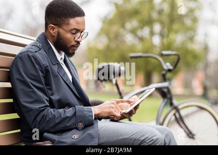 Gutaussehender Manager, der im Park an einem digitalen Tablet arbeitet Stockfoto