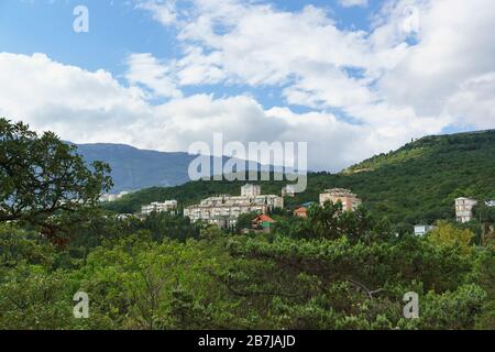 Blick auf die mehrgeschossigen Wohnhäuser an einem Berghang im Dorf Gaspra auf der Krim. Viel Grün im südlichen Resort Stockfoto