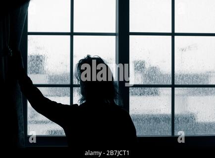 Frau, die am regnerischen Tag aus dem Fenster schaut. Bild des Verständigen; weibliche Depression, häuslicher Missbrauch, Selbstisolierung, Quarantäne, Coronavirus, Stockfoto