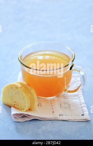 Frische, aus biologischem Anbau gefertigte goldene Hühnerknochen in durchsichtiger Glasschale mit Cibatta-Stockscheiben auf blauem Hintergrund in vertikalem Format. Konz für gesunde Ernährung Stockfoto