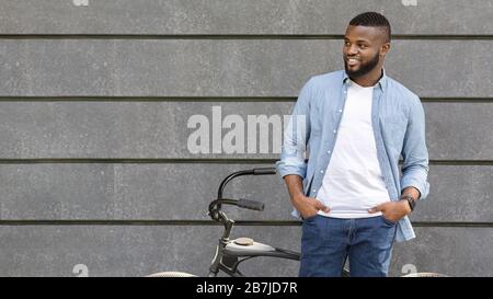 Schöner schwarzer Mann mit Fahrrad über grauem Wandhintergrund im Freien Stockfoto