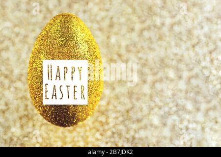 In der Luft hängt ein goldenes Ei. Auf einem strukturierten goldenen Hintergrund. Das Konzept zum Thema Ostern. Stockfoto