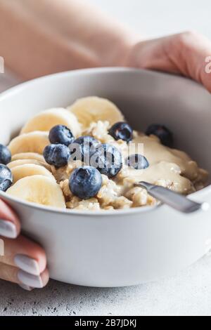 Haferbrei mit Blaubeeren, Bananen und Tahini in einer grauen Schüssel. Stockfoto