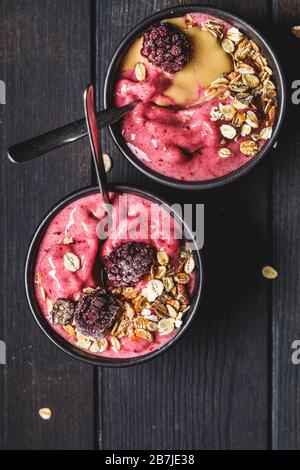 Vegane Beere Smoothie Schüssel mit Tahini und Müsli, dunkler Hintergrund. Hausgemachtes Beereneis mit Erdnussbutter und Granola. Stockfoto