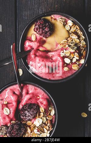 Vegane Beere Smoothie Schüssel mit Tahini und Müsli, dunkler Hintergrund. Hausgemachtes Beereneis mit Erdnussbutter und Granola. Stockfoto