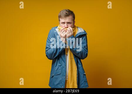 Der Mensch fühlt sich krank, er hat Fieber, er bedeckt den Mund mit einem Schal und hat Angst vor einem gefährlichen Virus, auf gelbem Hintergrund. Stockfoto