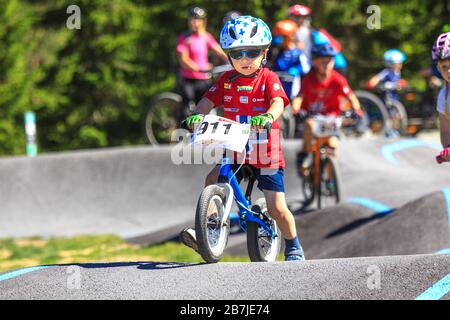 Kleiner Junge auf dem Gleichgewichtsfahrrad ohne Pedale, der am Radwettbewerb auf der Pumpenbahn teilnimmt. Stockfoto