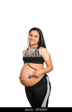 Nahaufnahme der schwangeren Frau mit Stethoskop am Bauch, das dem Baby zuhört. Schwangerschafts-, Lifestyle- und Mutterschaftskonzept. Stockfoto