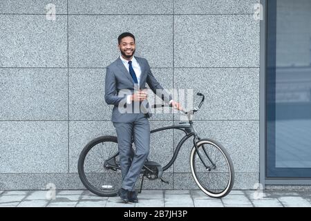 Ein gutaussehender afro-Geschäftsmann, der Kaffee und Fahrrad hält Stockfoto