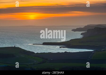 Kimmeridge, Dorset, Großbritannien. März 2020. Wetter in Großbritannien. Der Himmel leuchtet bei Sonnenuntergang von Swyre Head bei Kimmeridge an der Juraküste von Dorset aus orange und blickt nach einem Tag mit warmem Sonnenschein und klarem blauen Himmel nach Westen über die Kimmeridge Bay und die Warbarrow Bay. Bildnachweis: Graham Hunt/Alamy Live News Stockfoto