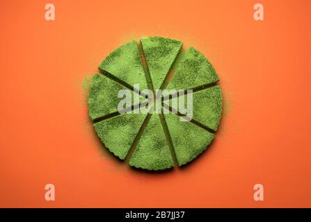 Matcha-Käsekuchen in Scheiben auf orangefarbenem, nahtlosem Hintergrund. Scheiben einer grünen Tart-Ebene lagen. Grünes Teepulver auf einem Kuchen. Stockfoto