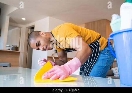 Nahaufnahme des jungen lateinmannes, der zu Hause Flecken vom Tisch entfernt. Reinigungs- und Reinigungskonzept. Stockfoto