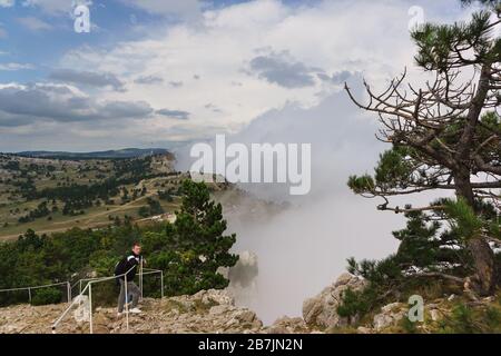 Von der Meeresküste steigt dichter Nebel auf den Gipfel des Mount AI-Petri, der als der nebeligste Ort auf der Krim gilt. Der Tourist befindet sich hinter der Bar Stockfoto