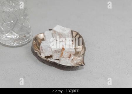 Lokum in metallischer Platte mit Glas Wasser auf Betongrund. Süße Speisen für Ramadan Stockfoto