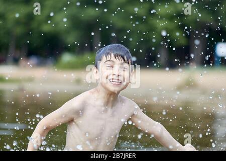 Der Junge spritzt im See fliegende Spritzer von Wasser. Stockfoto